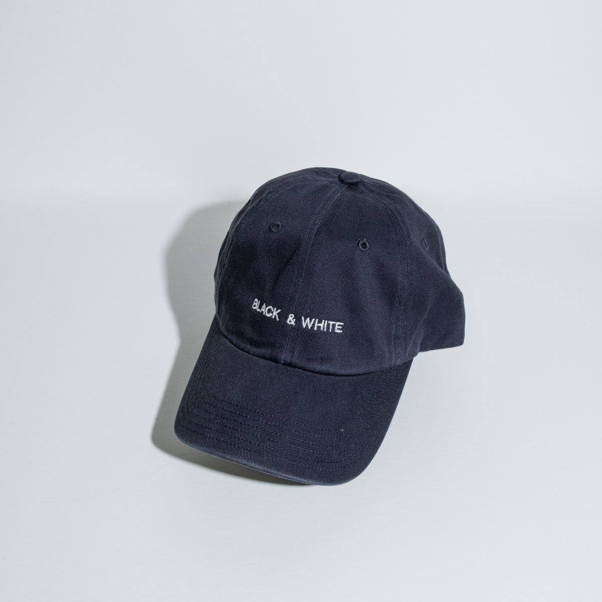 A dark navy blue cotton baseball cap with 'BLACK & WHITE' embroidered in white on the front, photographed on a clean white studio background.