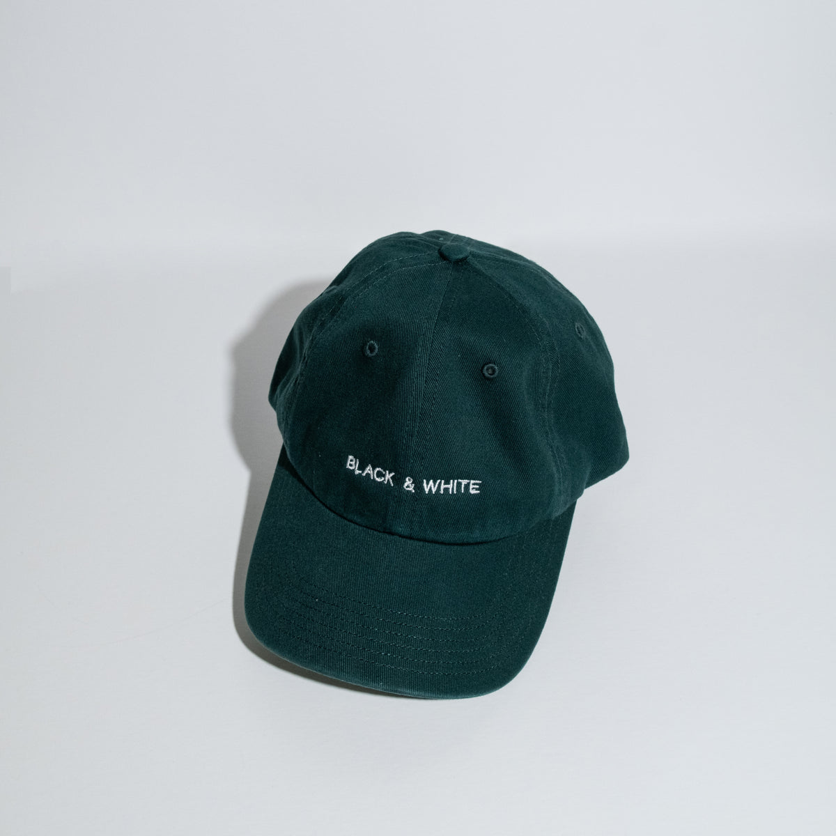 A dark forest green cotton baseball cap with 'BLACK & WHITE' embroidered in white on the front, displayed on a clean white surface against a white background.