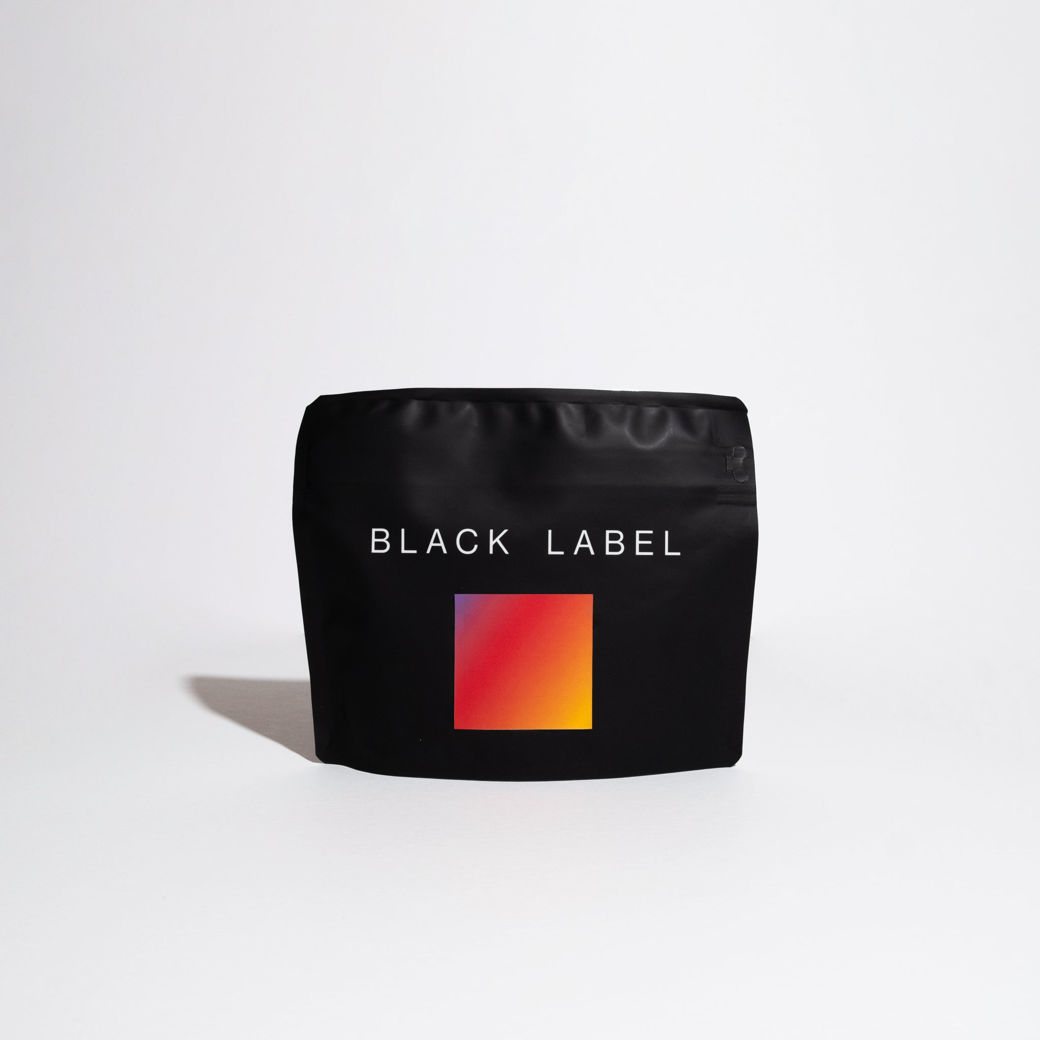 Matte-black pouch labeled BLACK LABEL with red-to-orange swatch, representing Finca Deborah Symmetry coffee. Showcases top-tier Panamanian Gesha production by Jamison Savage.
