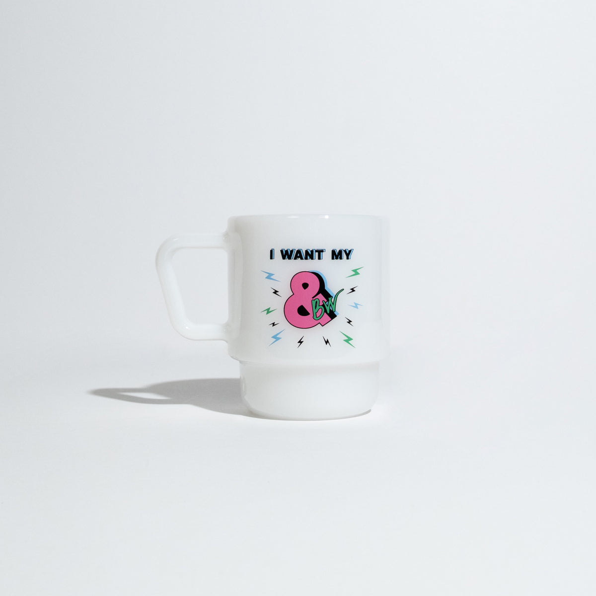 A white ceramic mug with a handle, featuring a graphic of a pink pear with the text 'I WANT MY B&W' in black and colorful dots, set against a plain white background.
