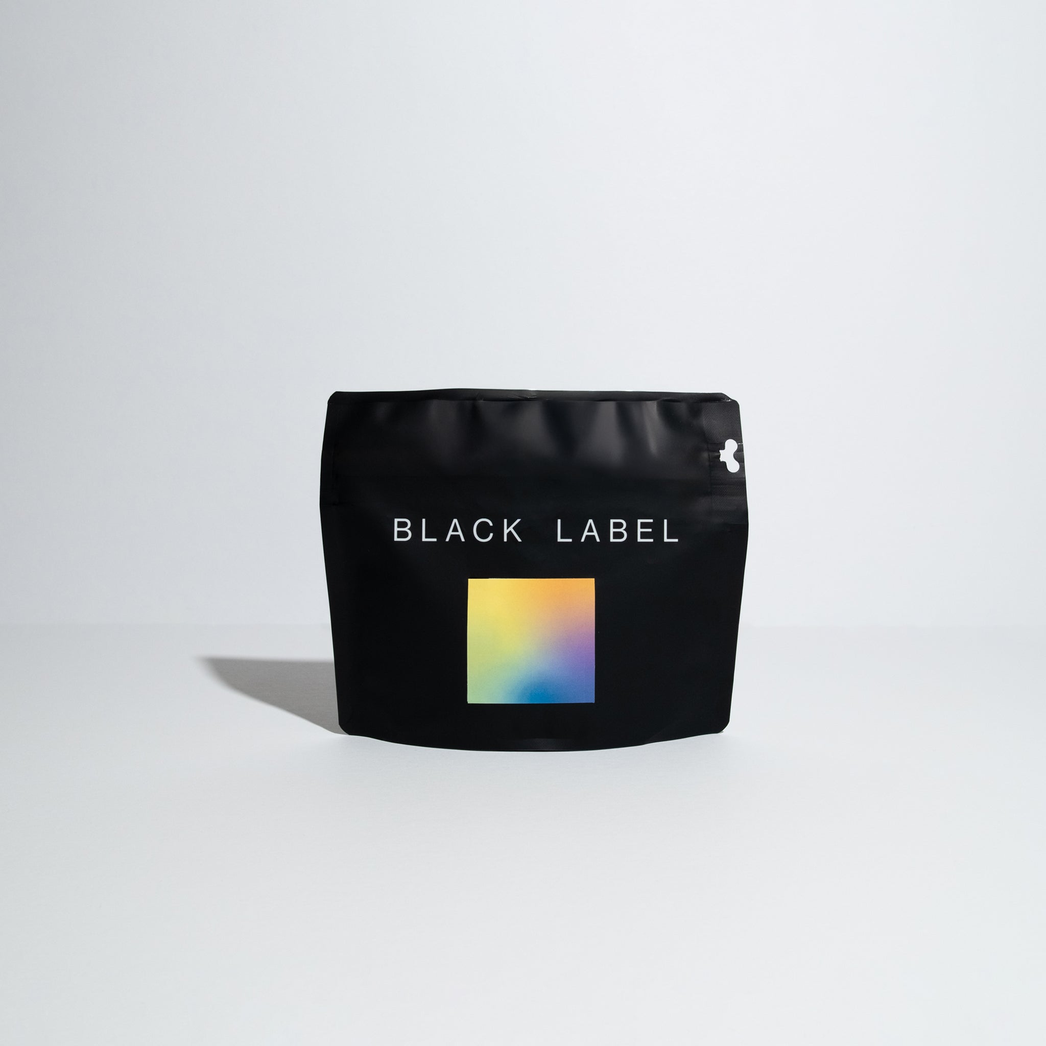 A black bag with the words "Black Label" written in a sans serif modern font covering around 75% of the top portion of the bag. In the center of the black bag is a square label with a morpheus gradient with the colors of light yellow to tangerine orange to a lime green and blue purple. 