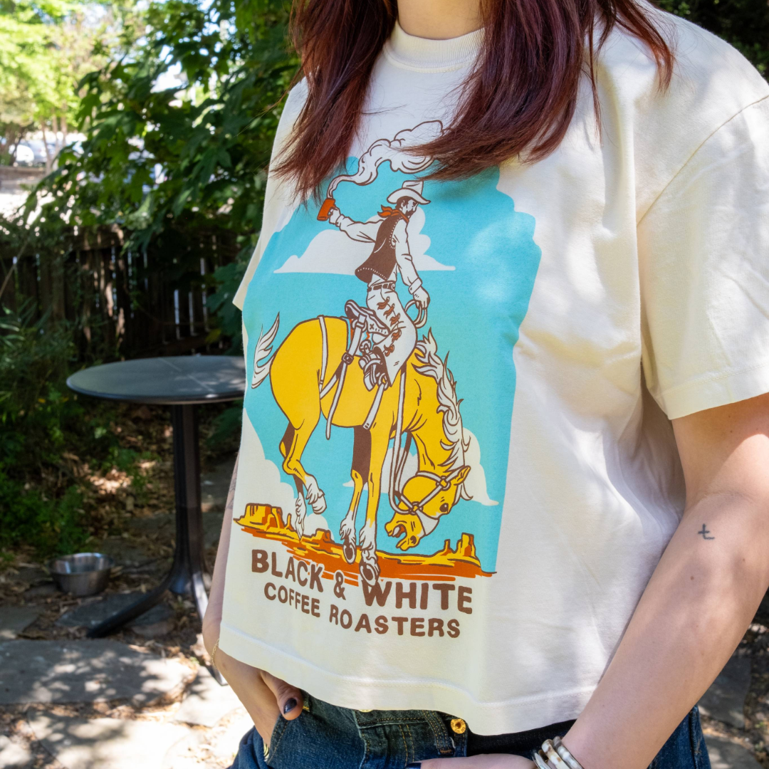 Person wearing a t-shirt with a graphic design of a cowboy on a horse and text 'Black & White Coffee Roasters'.