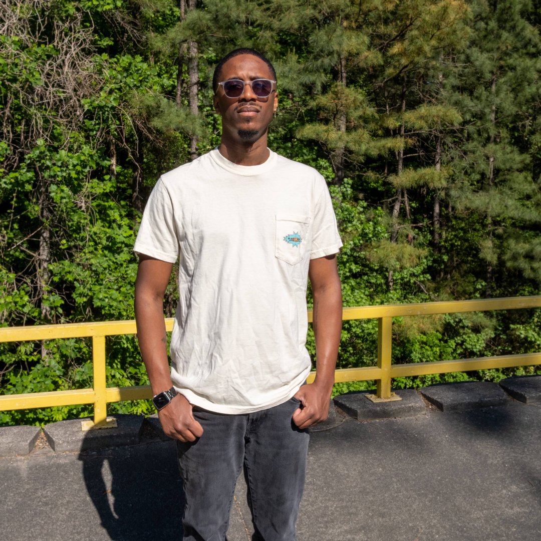 Man wearing Cowboy Pocket Tee, featuring a small graphic on the left chest pocket, sunglasses, dark pants, and a smartwatch, standing outdoors.