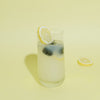 A video of a glass of lemonade with lemons and blackberries floating in it and a hand coming into frame and setting a slice of lemon on the edge of the glass. 
